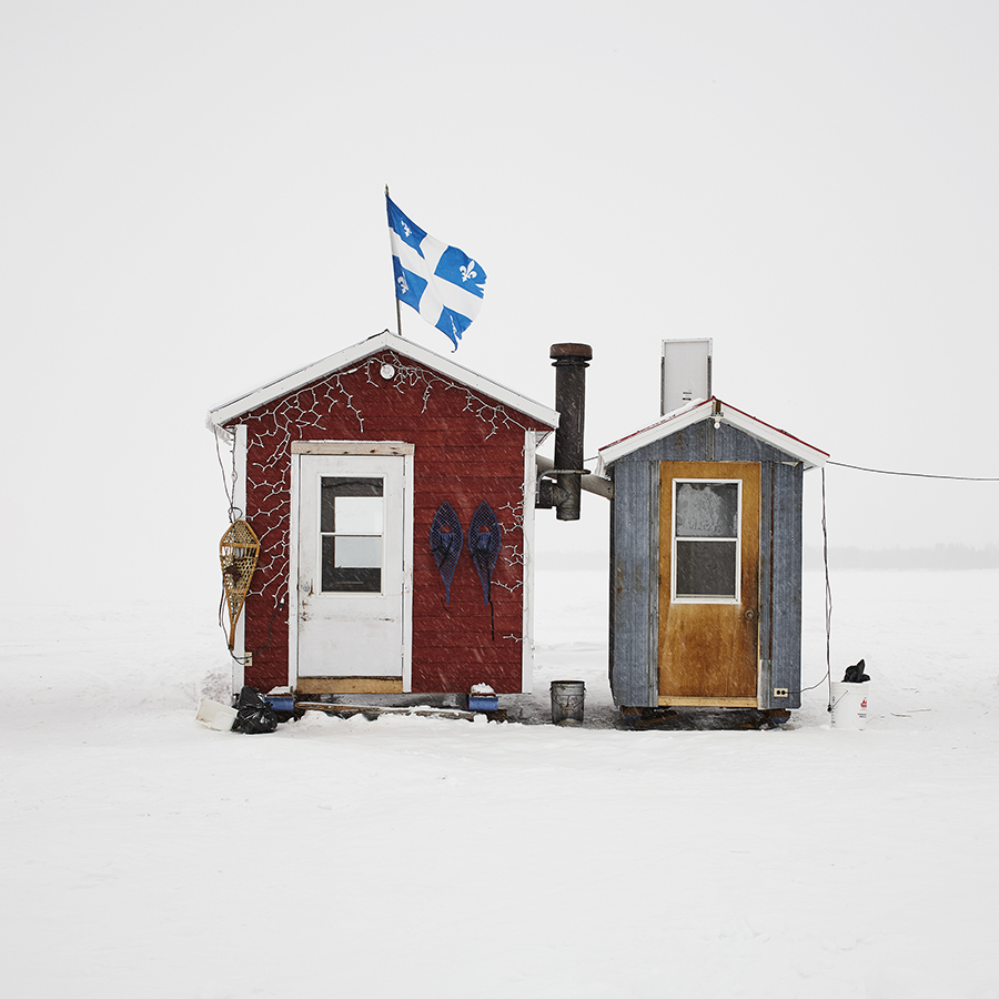 Two adjacent fishing huts, one with a Quebec flag on top